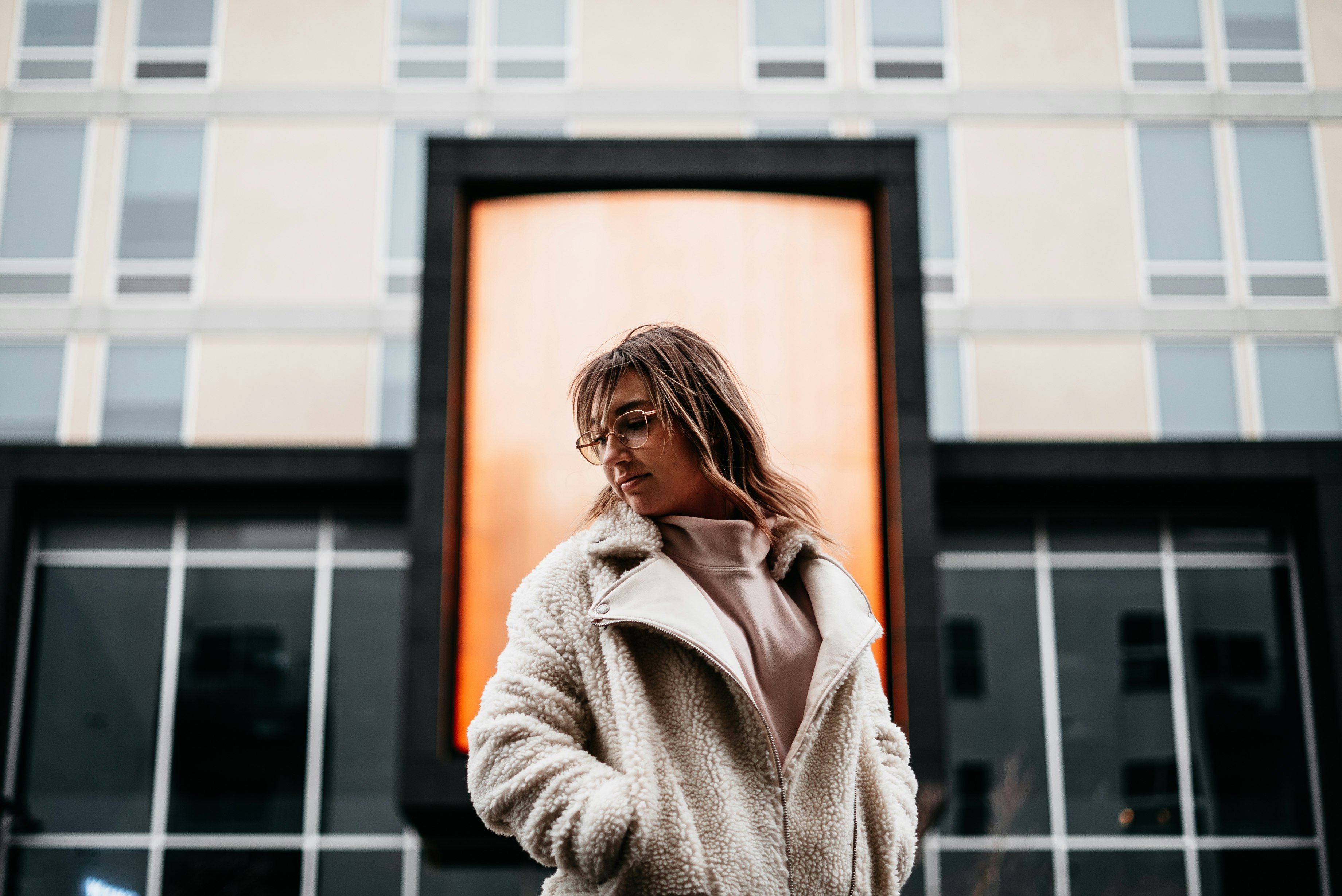 woman in beige coat standing near glass window during daytime